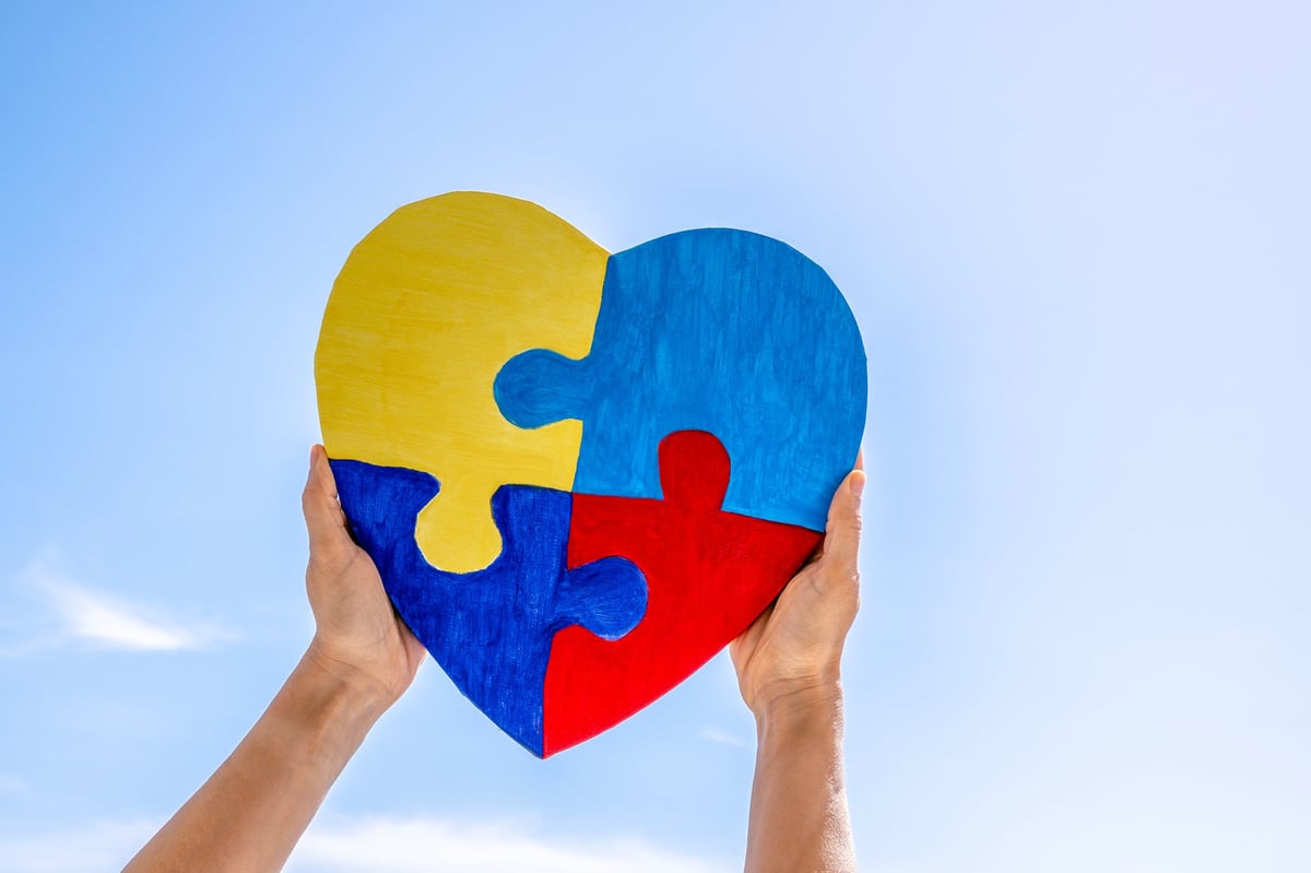 World autism awareness day, Autism spectrum disorder concept. Adult and child hands holding together colorful painted puzzle heart on blue sky background.
