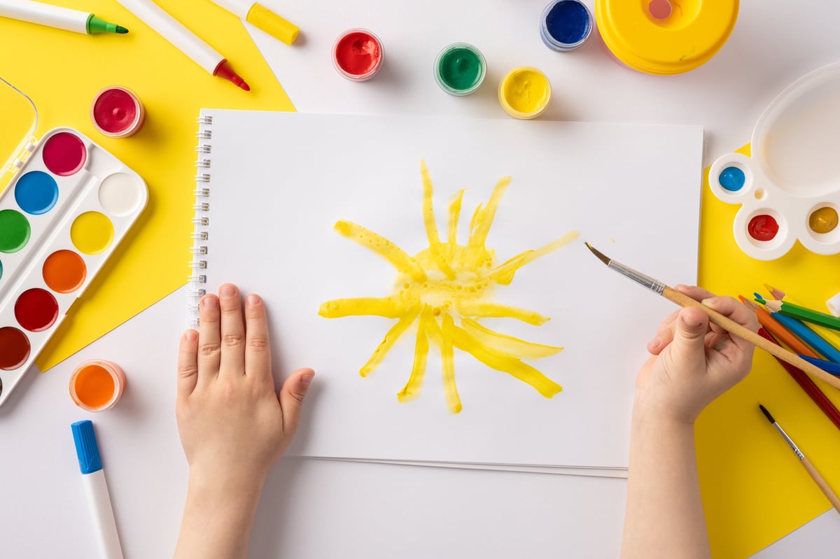 A child engages in creative painting, drawing a sun with yellow paint with colorful art supplies