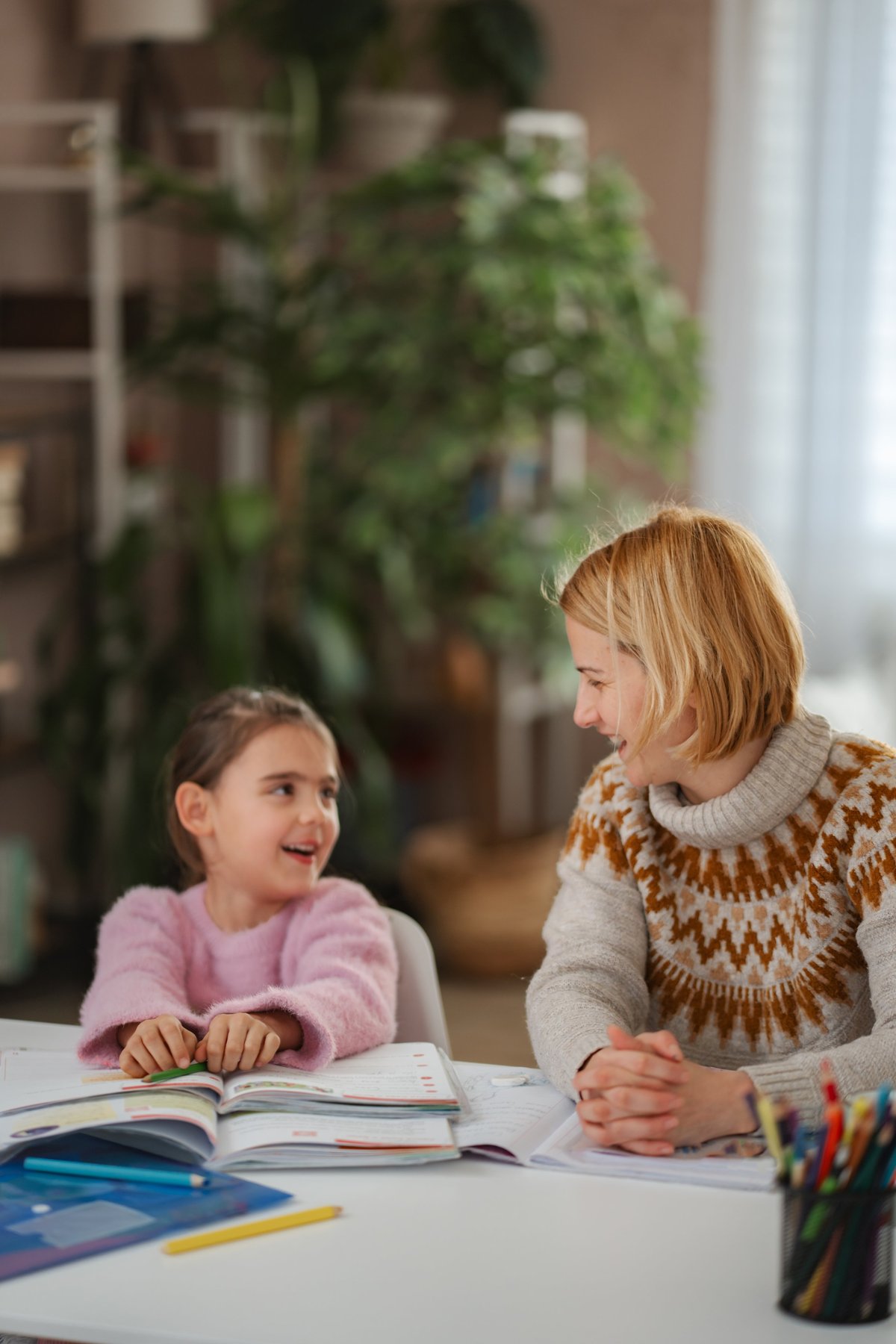 White mother helping daughter with school homework at home enjoying education
