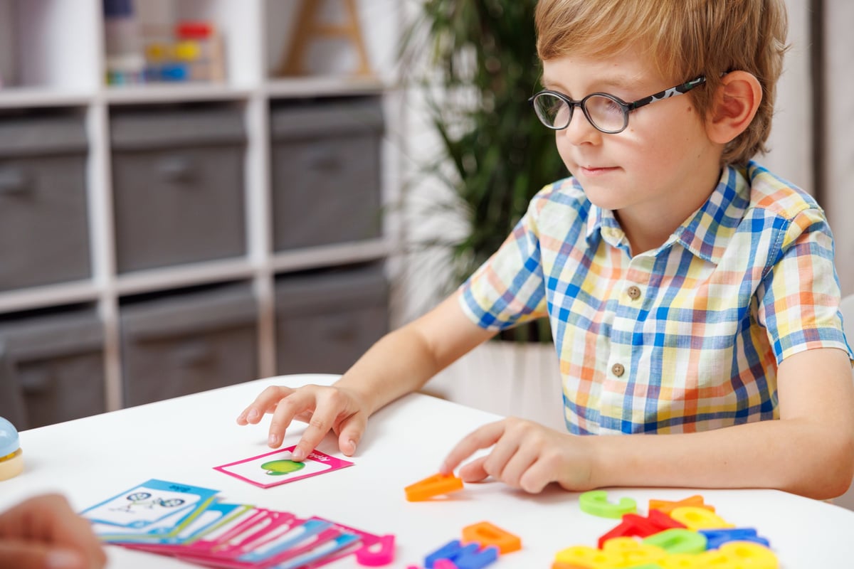 A young boy wearing glasses and a colorful plaid shirt playing with educational cards