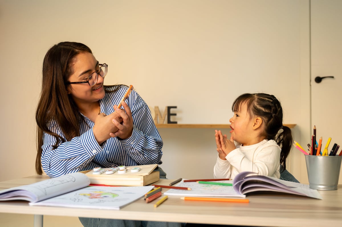 Teacher and preschooler interacting during a learning activity at a classroom table